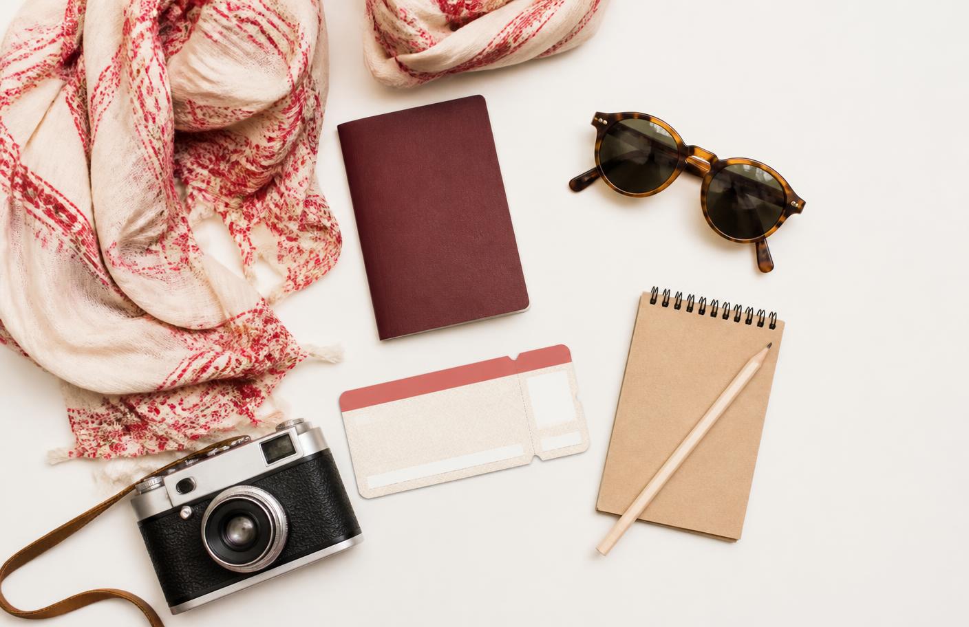 Travel essentials laid out: passport, scarf, sunglasses, notebook and camera